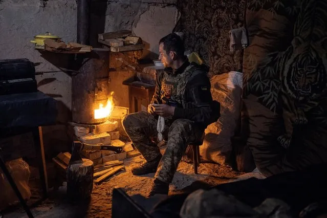 A Ukrainian serviceman of the 80th Independent Air Assault Brigade warms by the fire at their base, as Russia's attack on Ukraine continues, near the frontline town of Bakhmut, Donetsk region, Ukraine on February 24, 2023. (Photo by Marko Djurica/Reuters)