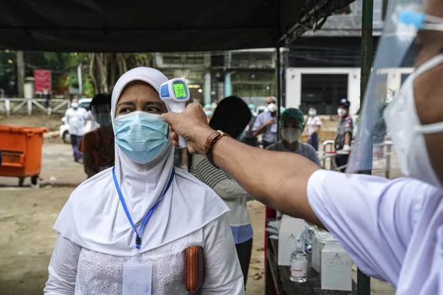 A woman gets her temperature checked before entering a polling station Sunday, November 8, 2020, in Yangon, Myanmar. (Photo by Aung Naing Soe/AP Photo)