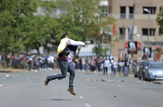 A student hurls a stone off the University of the Witwatersrand campus in Johannesburg South Africa on Monday, October 10, 2016. Tear gas and water cannon were fired as hundreds of students protested at the university amid a bitter national dispute with university managers and the government over demonstrators' demands for free education. (Photo by AP Photo)