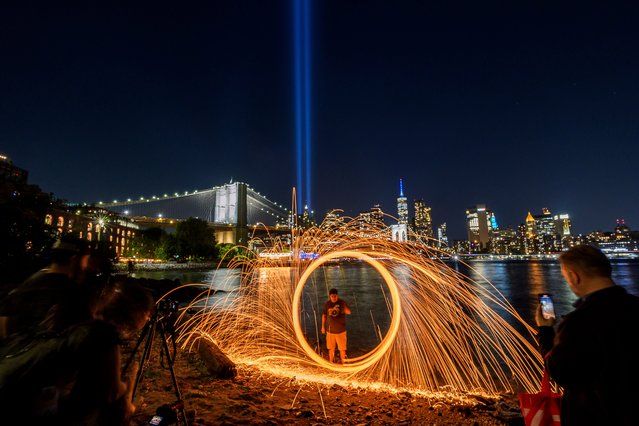 A person spins steel wool as the annual Tribute in Light shines in the sky behind the Brooklyn Bridge, Thursday, September 11, 2025, in the Brooklyn borough of New York. (Phoot by Adam Gray/AP Photo)