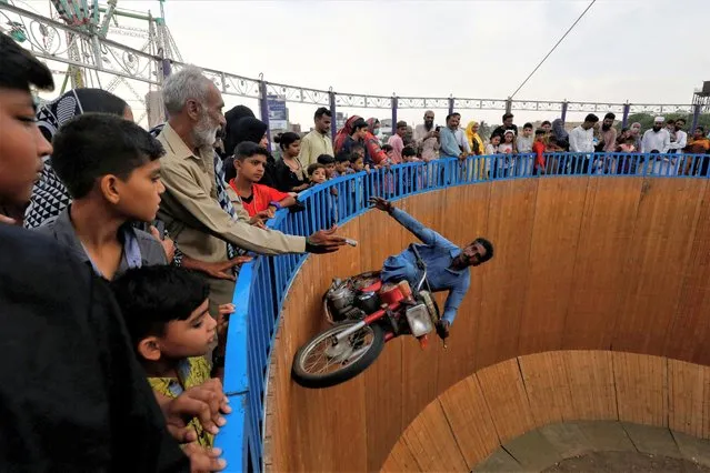 A performer extends his hand to grasp money from the audience, while riding a motorbike with one leg up on the walls of the “Well of Death”, at a fair in Karachi, Pakistan on April 24, 2023. (Photo by Akhtar Soomro/Reuters)