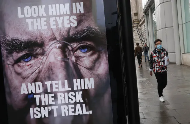 A man wearing a mask against coronavirus walks past an NHS advertisement about COVID-19 in London, Tuesday, February 2, 2021. British health authorities plan to test tens of thousands of people in a handful of areas of England in an attempt to stop a new variant of the coronavirus first identified in South Africa spreading in the community. The Department of Health says a small number of people in England who had not travelled abroad have tested positive for the strain. (Photo by Alastair Grant/AP Photo)