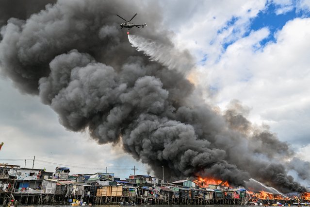 A Philippine Air Foce helicopter drops water over houses on fire at Tondo in Manila on November 24, 2024. Raging orange flames and thick black smoke billowed into the sky, as fire ripped through hundreds of houses in a closely built slum area of the Philippine capital Manila. (Photo by Jam Sta Rosa/AFP Photo)