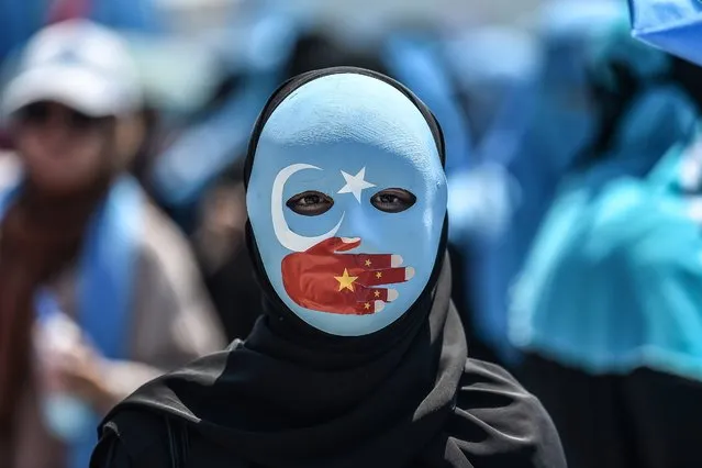 A demonstrator wearing a mask painted with the colours of the flag of East Turkestan and a hand bearing the colours of the Chinese flag attends a protest of supporters of the mostly Muslim Uighur minority and Turkish nationalists to denounce China's treatment of ethnic Uighur Muslims during a deadly riot in July 2009 in Urumqi, in front of the Chinese consulate in Istanbul, on July 5, 2018. Nearly 200 people died during a series of violent riots that broke out on July 5, 2009 over several days in Urumqi, the capital city of the Xinjiang Uyghur Autonomous Region, in northwestern China, between Uyghurs and Han people. (Photo by Ozan Kose/AFP Photo)