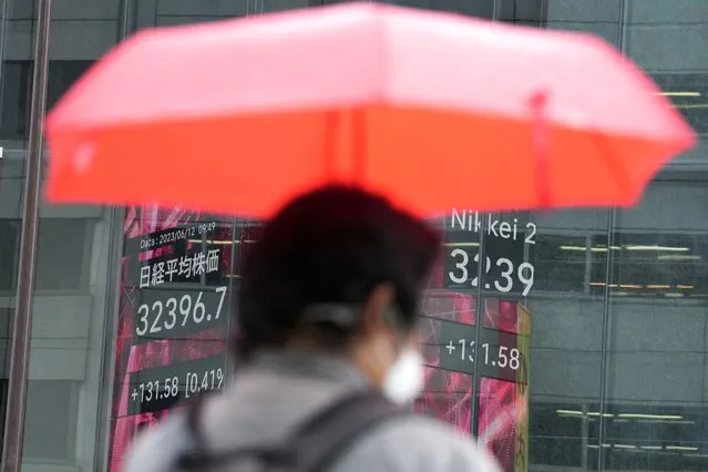 A person holding an umbrella in the rain walks in front of an electronic stock board showing Japan's Nikkei 225 index at a securities firm Monday, June 12, 2023, in Tokyo. Shares were mixed in Asia on Monday after the S&P 500 logged its fourth winning week in a row, while investors await another decision by the Federal Reserve on interest rates.(Photo by Eugene Hoshiko/AP Photo)