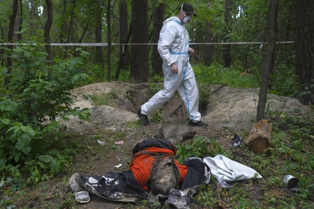A member of an extraction crew walks near a body found in the woods during an exhumation of a mass grave near Bucha, on the outskirts of Kyiv, Ukraine, Monday, June 13, 2022. (Photo by Natacha Pisarenko/AP Photo)