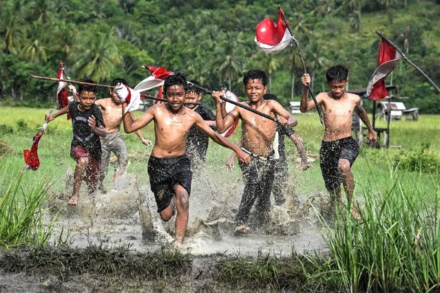 Boys run in a field with flags of Indonesia during an event of traditional games on the eve of Indonesia's 78th Independence Day at the Nusa tourism village, Aceh province, on August 16, 2023. (Photo by Chaideer Mahyuddin/AFP Photo)