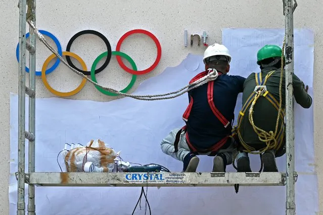 Labourers work beside the Olympic signage at the entrance of a venue ahead of the upcoming 141st International Olympic Committee (IOC) session in Mumbai on OCtober 11, 2023. (Photo by Indranil Mukherjee/AFP Photo)