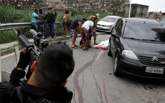 A police officer is seen as Fabiana Cardoso Domingues reacts near the body of her son, Anderson Domingues, after he was shot dead during an operation against drug gangs in the Alemao slums complex in Rio de Janeiro, Brazil, October 1, 2018. (Photo by Ricardo Moraes/Reuters)