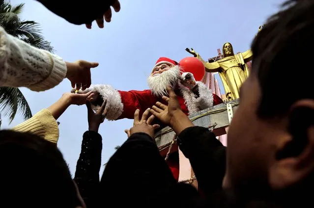A man dressed as Santa Claus distributes sweets to children on the occasion of Christmas outside a church in Gauhati, India, Wednesday, December 25, 2013. Although Christians comprise only two percent of the population among a Hindu majority, the holiday is observed across the country as an occasion to celebrate. (Photo by Anupam Nath/AP Photo)