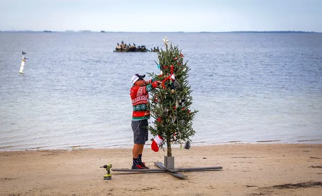 Mike Womack, 52, puts the final touches on a Christmas tree along Sunset Beach Sunday, December 24, 2023 in Tarpon Springs, Fla. For the past nine years Womack has set up a tree along the beach for local residents to enjoy. (Photo by Chris Urso/Tampa Bay Times via AP Photo)