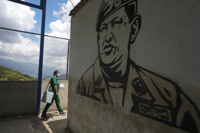 Nurse Genny Zorrilla walks with a cooler containing Sinopharm COVID-19 vaccines past a mural of late president Hugo Chavez, during house to house vaccinations in the popular neighborhood of El Valle in Caracas, Venezuela, Monday, September 27, 2021. According to the Pan American Health Organization Venezuela one of the least vaccinated countries in the continent, is seeing a growing uptick in caseloads, unlike other countries in the region where cases are dropping. (Photo by Ariana Cubillos/AP Photo)