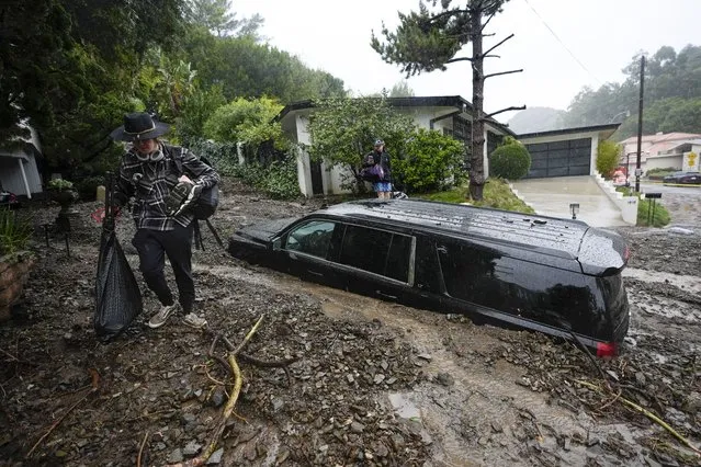 Residents evacuate past damaged vehicles after storms caused a mudslide, Monday, February 5, 2024, in the Beverly Crest area of Los Angeles. A storm of historic proportions unleashed record levels of rain over parts of Los Angeles on Monday, endangering the city's large homeless population, sending mud and boulders down hillsides dotted with multimillion-dollar homes and knocking out power for more than a million people in California. (Photo by Marcio Jose Sanchez/AP Photo)