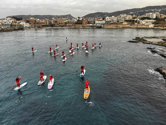 An aerial view shows people dressed with Santa Claus outfits riding on standup paddles in the Mediterranean Sea, in Lebanon's northern coastal city of Batroun on December 21, 2023. (Photo by Ibrahim Chalhoub/AFP Photo)