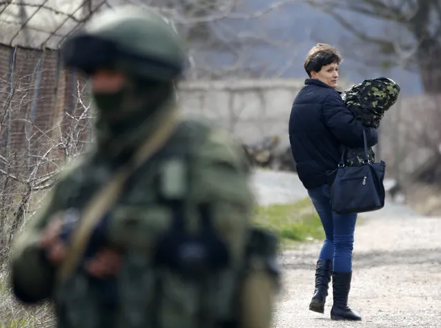 A woman, believed to be a Ukrainian servicewoman, carrying her uniform looks back at an armed man, believed to be a Russian serviceman, while leaving a military base in Perevalnoye, near the Crimean city of Simferopol, March 19, 2014. Ukraine's National Security and Defence Council opened a session on Wednesday devoted to threats to national security following Russia's moves to take control of the Crimea peninsula. (Photo by Shamil Zhumatov/Reuters)