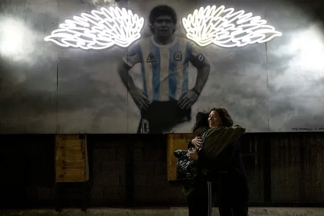 Women hug near a mural of the late soccer star Diego Maradona in Buenos Aires, Argentina, late Tuesday, November 23, 2021. The first anniversary of the soccer legend's death is on Nov. 25. (Photo by Rodrigo Abd/AP Photo)