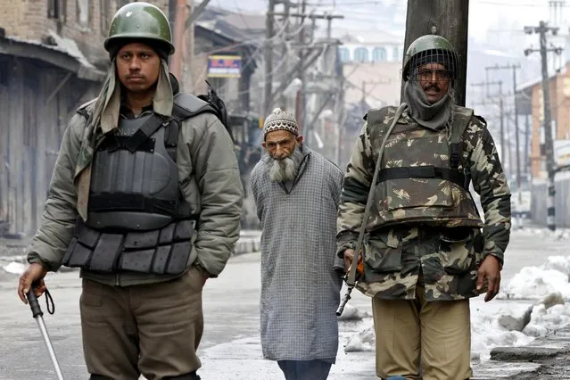An elderly Kashmiri civilian walks as Indian paramilitary soldiers stand guard during restrictions in Srinagar, India, Sunday, March 16, 2014 Kashmiri separatists called for a strike Sunday to protest the killing of a teenager boy by government forces in the troubled Indian portion of Kashmir. (Photo by Mukhtar Khan/AP Photo)