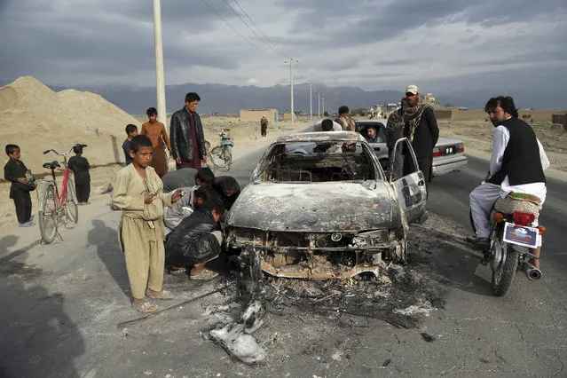 Afghans watch a civilian vehicle burnt after being shot by US forces after an attack near the Bagram Air Base, north of Kabul, Afghanistan, Tuesday, April 9, 2019. Three American service members and a U.S. contractor were killed when their convoy hit a roadside bomb on Monday near the main U.S. base in Afghanistan, the U.S. forces said. The Taliban claimed responsibility for the attack. (Photo by Rahmat Gul/AP Photo)