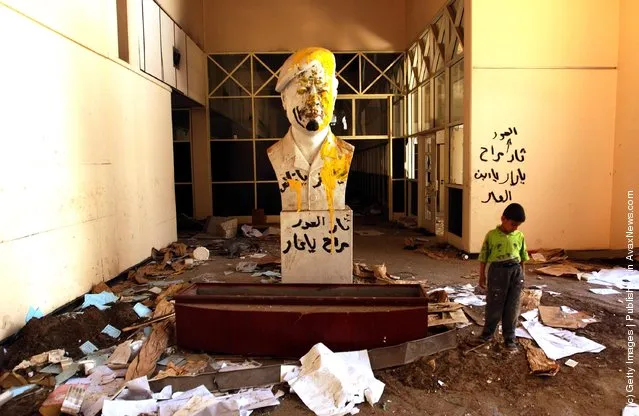 A boy walks past a vandalized Saddam Hussein statue