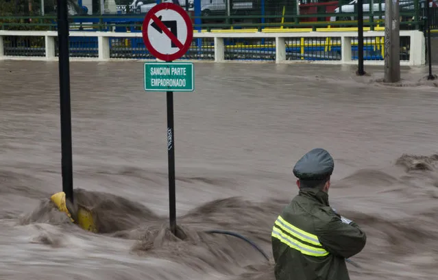 A National Police officer stands next to a flooded street in Santiago, Chile, Sunday, April 17, 2016. Authorities say the Rio Mapocho flooded several districts of the city and landslides killed at least one person. (Photo by Esteban Felix/AP Photo)