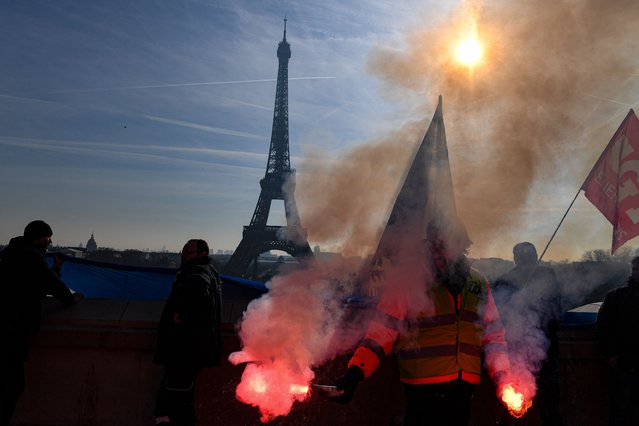 A members of the SUD labour union holds flares during a demonstration on the Parvis du Trocadero, across the Seine river from the Eiffel Tower, during a cross-sector labour union protest against France's controversial pension reform bill, in Paris, on February 9, 2023. The planned reforms include hiking the retirement age from 62 to 64 and increasing the number of years people must make contributions for a full pension. (Photo by Alain Jocard/AFP Photo)