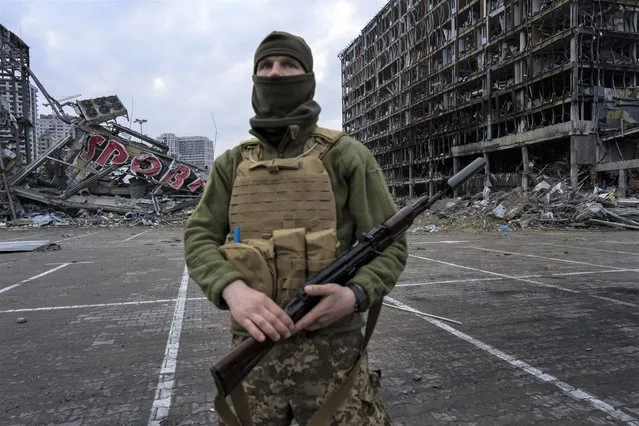 A soldier poses for the picture in Kyiv, Ukraine, Wednesday, March 30, 2022, while standing guard amid the destruction caused after shelling of a shopping center on March 21. (Photo by Rodrigo Abd/AP Photo)