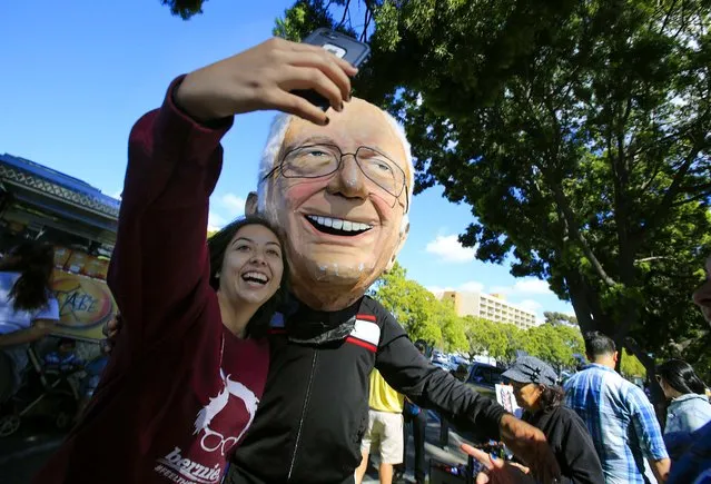 Bernie Sanders supporter Arely Ramos of Chula Vista takes a self with Mike Johnson of Linda Vista, wearing a paper mache Bernie Sanders head while they wait for the doors to the rally in Kimball Park to open Saturday, May 21, 2016 in National City, Calif. (Photo by Howard Lipin/The San Diego Union-Tribune via AP Photo)