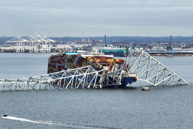 In this aerial image, the steel frame of the Francis Scott Key Bridge sits on top of a container ship after the bridge collapsed, Baltimore, Maryland, on March 26, 2024. The bridge collapsed early March 26 after being struck by the Singapore-flagged Dali container ship, sending multiple vehicles and people plunging into the frigid harbor below. There was no immediate confirmation of the cause of the disaster, but Baltimore's Police Commissioner Richard Worley said there was “no indication” of terrorism. (Photo by Jim Watson/AFP Photo)