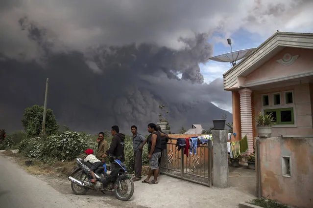 Villagers gather in front of a house as they watch Mount Sinabung releasing a pyroclastic flow during its eruption in Karo, North Sumatra, Indonesia, Wednesday, August 2, 2017. The volcano blasted volcanic ash as high as 4.2 kilometers (2.6 miles), one of its biggest eruptions in the past several months of high activity. (Photo by Endro Rusharyanto/AP Photo)