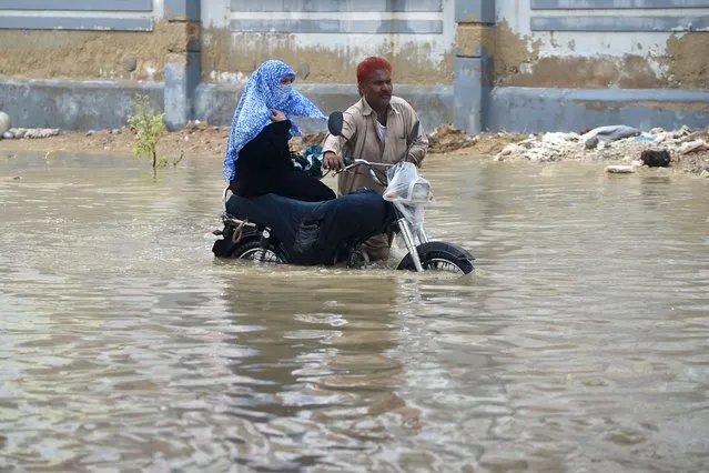 Commuters wade through a flooded street after a heavy rain shower in Karachi on July 11, 2022. (Photo by Rizwan Tabassum/AFP Photo)