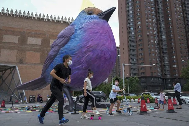 Residents wearing face masks walk by a giant bird structure on display outside an art gallery in Beijing, Monday, August 8, 2022. (Photo by Andy Wong/AP Photo)