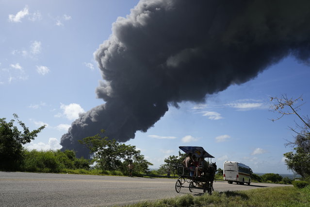A carriage and bus drive past a plume of smoke caused by a blaze at the Matanzas Supertanker Base, in Matazanas, Cuba, Saturday, August 6, 2022. (Photo by Ramon Espinosa/AP Photo)