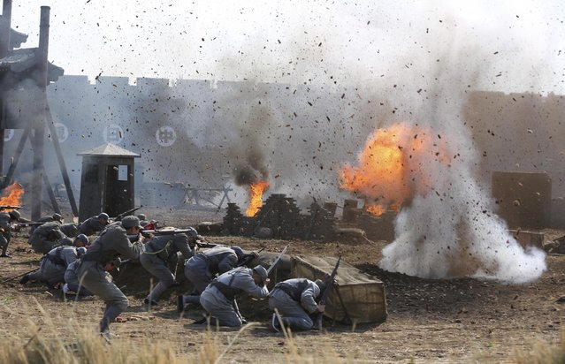 Performers and tourists dressed in military costumes hide behind a barrier near an explosion site, as a battle scene between China and Japan is performed at a film city in Shenyang, Liaoning province September 24, 2014. (Photo by Reuters/Stringer)