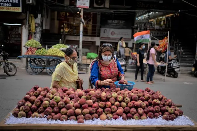 Women wearing masks as a precaution against the coronavirus buy apples from a roadside vendor in New Delhi, India, Thursday, August 11, 2022. (Photo by Altaf Qadri/AP Photo)