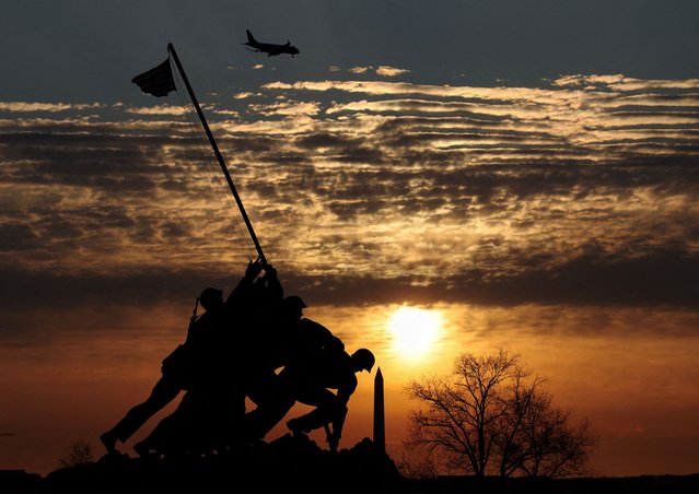 A plane flies overhead as the sun rises behind the Washington Monument and the U.S. Marine Corps War Memorial (Iwo Jima Memorial) on the first day of spring in Arlington, Virginia on March 20, 2025. (Photo by Kevin Lamarque/Reuters)
