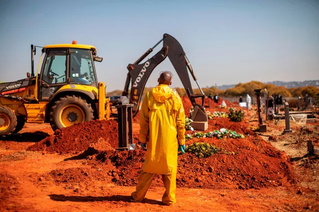 An undertaker wearing personal protective equipment (PPE) overwatches as an excavator fills with soil the grave containing the remains of Modise Motlhabane, who died of COVID-19 coronavirus, during the funeral at the Westpark cemetery in Johannesburg, on July 22, 2020. (Photo by Michele Spatari/AFP Photo)