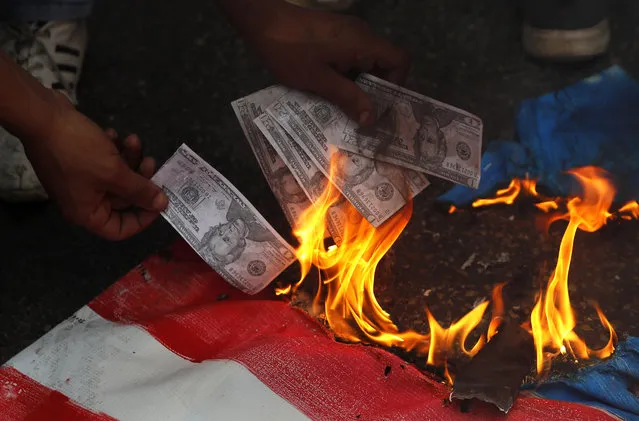 A supporter of a communist group burns representation of U.S. currency, during a protest against U.S. interference in Lebanon's affairs, near the U.S. embassy, in Aukar northeast of Beirut, Lebanon, Friday, July 10, 2020. (Photo by Hussein Malla/AP Photo)