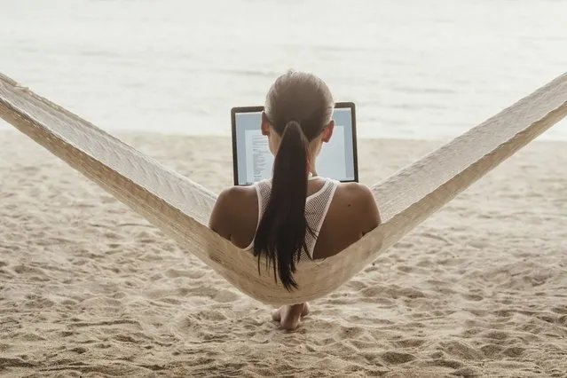 Rear view of woman using laptop computer while relaxing on hammock in Thailand. (Photo by Cavan Images via Getty Images)