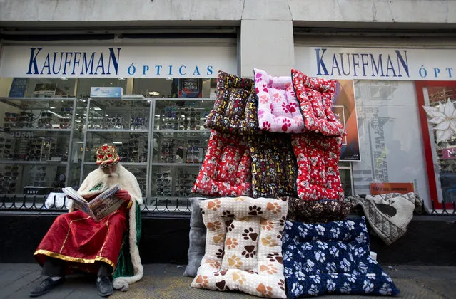 Performance artist Roberto Martinez Perez, dressed as one of the Three Kings, reads a newspaper while waiting for families wanting to pose for souvenir photos on the eve of the Epiphany, in the historic center of Mexico City, Friday, January 5, 2018. In Mexico, it is customary for people to give gifts on Three Kings Day also known as the Epiphany, commemorated on Jan. 6. According to Christian tradition, Jan. 6 marks the arrival of three wise men bearing gifts for the baby Jesus. (Photo by Rebecca Blackwell/AP Photo)