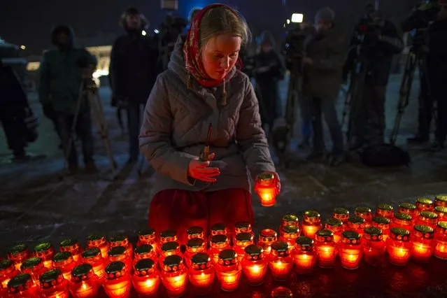 A girl places a candle as a group gather at the Cathedral of Christ the Savior in Moscow to light 71 candles in memory of those killed in the An-148 plane crash, on Monday, February 12, 2018.  A Russian passenger plane carrying 71 people crashed Sunday near Moscow, killing everyone aboard shortly after the jet took off from one of the city's airports. The Saratov Airlines regional jet disappeared from radar screens a few minutes after departing from Domodedovo Airport en route to Orsk, a city some 1,500 kilometers (1,000 miles) southeast of Moscow. (Photo by Alexander Zemlianichenko/AP Photo)