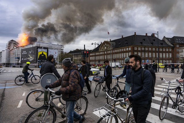 People ride bicycles as smoke rises from the Old Stock Exchange in Copenhagen, Denmark, Tuesday, April 16, 2024. A fire raged through one of Copenhagen’s oldest buildings on Tuesday, causing the collapse of the iconic spire of the 17th-century Old Stock Exchange as passersby rushed to help emergency services save priceless paintings and other valuables. (Photo by Emil Nicolai Helms/Ritzau Scanpix via AP Photo)