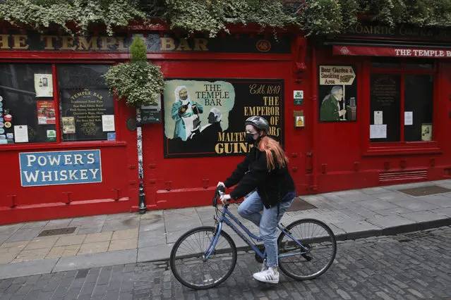 A cyclist passes a closed bar in the Temple bar area of Dublin, Ireland, Wednesday, October 21, 2020. With COVID-19 cases on the rise, the government has imposed a tough new lockdown, shutting down non-essential shops, limiting restaurants to takeout service and ordering people to stay within five kilometers (three miles) of their homes for the next six weeks. (Photo by Peter Morrison/AP Photo)