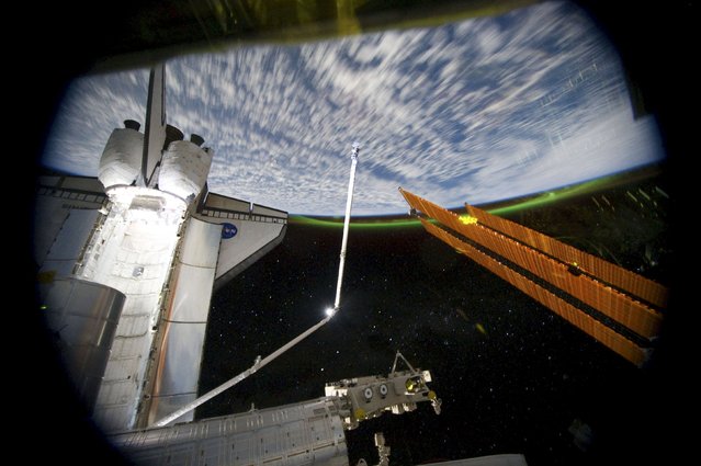 The Aurora Australis or the Southern Lights can be seen on the Earth's horizon in this panoramic view from the International Space Station looking past the docked space shuttle Atlantis' cargo bay on July 14, 2011, in this NASA handout image. (Photo by Reuters/NASA)