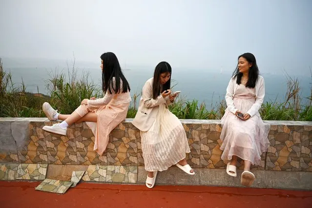 Women sit on a wall overlooking the Taiwan strait on Pingtan island, in China's southeast Fujian province on April 14, 2023. (Photo by Greg Baker/AFP Photo)