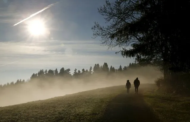 People walk along a forest as the sun shines over fog near Albis Pass mountain pass, Switzerland November 12, 2015. (Photo by Arnd Wiegmann/Reuters)