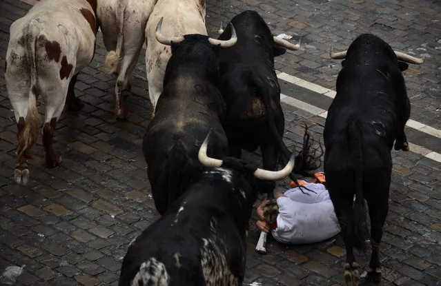Bulls run over a reveller during the first running of the bulls of the San Fermin festival in Pamplona, Spain, July 7, 2018. (Photo by Vincent West/Reuters)