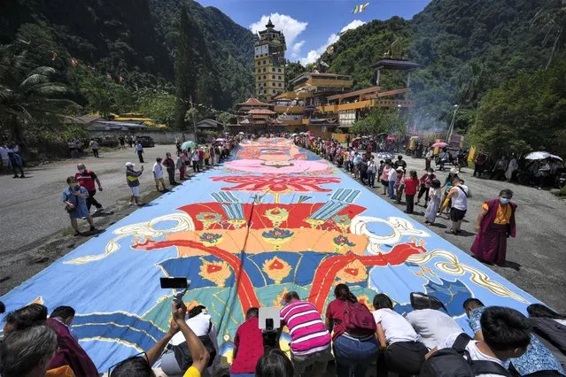 Devotees unveil a giant canvas of sacred “Thangka” measuring 60 meters (197 feet) by 12 meters (39 feet), under the sun during Wesak day celebration in Ipoh, Malaysia, Thursday, May 4, 2023. Wesak Day, one of the holiest days for Buddhists, offers an opportunity for all followers to come together and celebrate not only Buddha's birthday, but also his enlightenment and achievement of nirvana. (Photo by Vincent Thian/AP Photo)
