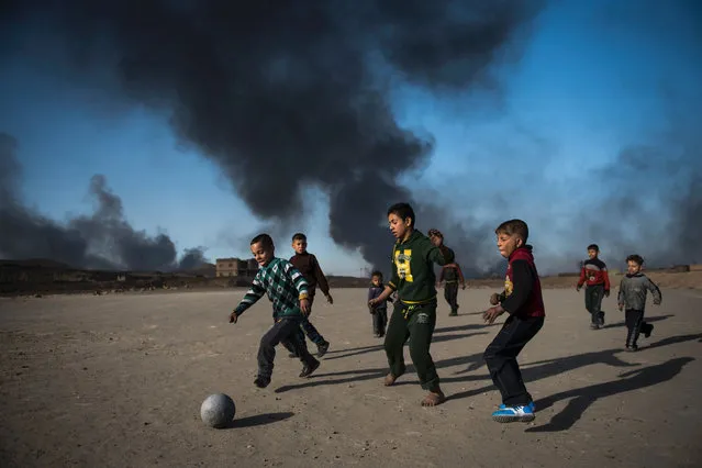 Children play football as oil wells, set ablaze by retreating Islamic State (IS) jihadists, burn behind them in the town of Qayyarah, some 70 km south of Mosul on November 20, 2016. Locals told AFP that they face a range of health issues including breathing difficulties, and sheperds said they could not sell their livestock as the sheep's fleece was blackened by smoke. (Photo by Odd Andersen/AFP Photo)