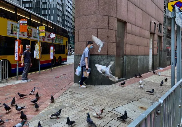 A man wearing face mask to help protect against the spread of the coronavirus walks past some flying pigeon at a street in Hong Kong, Monday, April 26, 2021. (Photo by Vincent Yu/AP Photo)