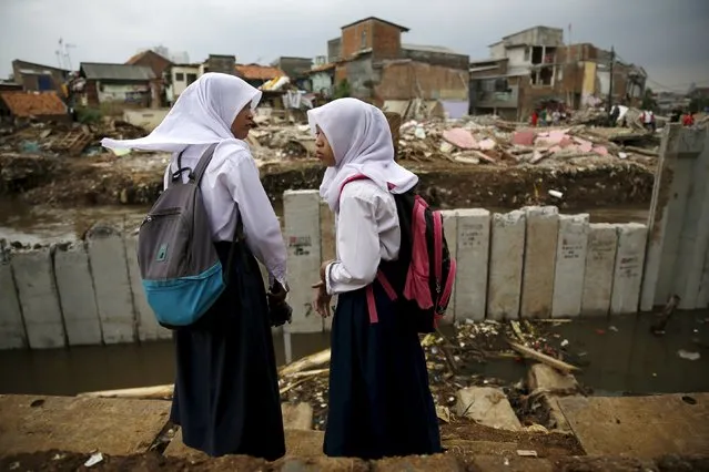 Schoolchildren stand near concrete floodwall as government officials demolish houses on the banks of Ciliwung river in Jakarta, Indonesia January 12, 2016. More than 60 residential buildings were demolished by the authorities to give way to a flood mitigation project along the river, local media reported on Tuesday. (Photo by Reuters/Beawiharta)
